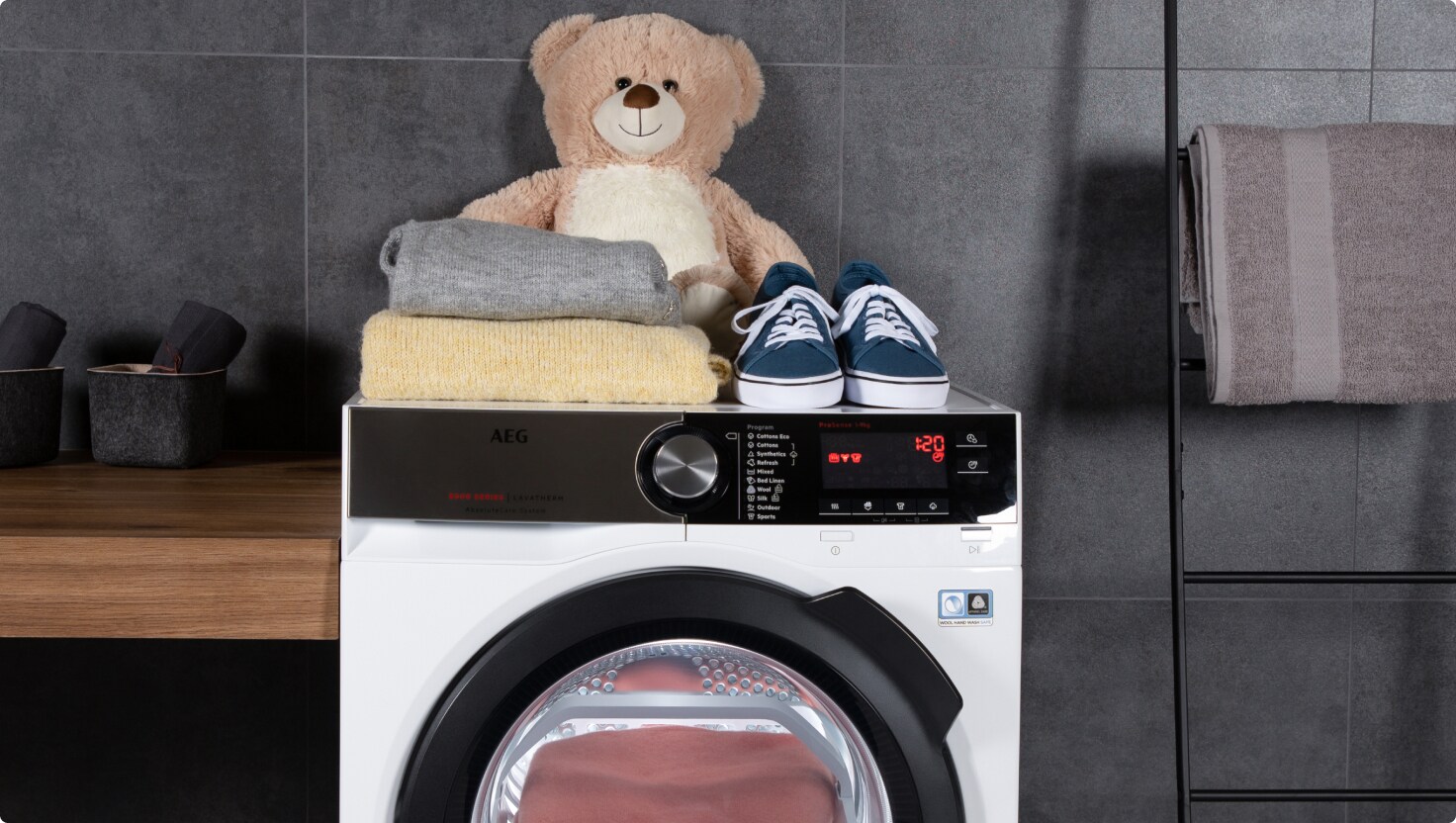 Teddy bear, sweaters and a pair of shoes placed on top of an AEG washing machine .